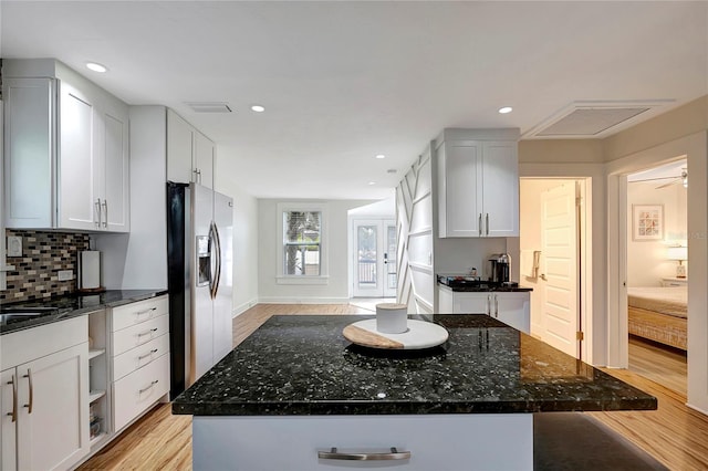 kitchen featuring light wood finished floors, a kitchen island, stainless steel refrigerator with ice dispenser, and dark stone counters
