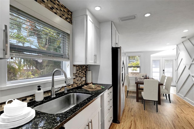 kitchen with a sink, stainless steel fridge, visible vents, backsplash, and light wood-style floors