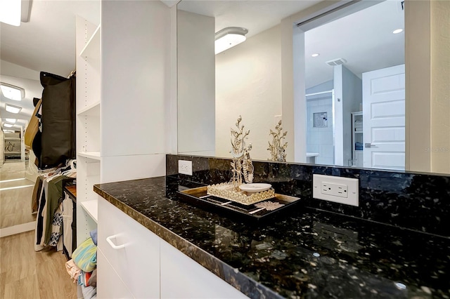 bathroom with a spacious closet, vanity, wood finished floors, and visible vents