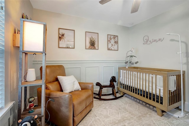 bedroom featuring a nursery area, a wainscoted wall, and ceiling fan