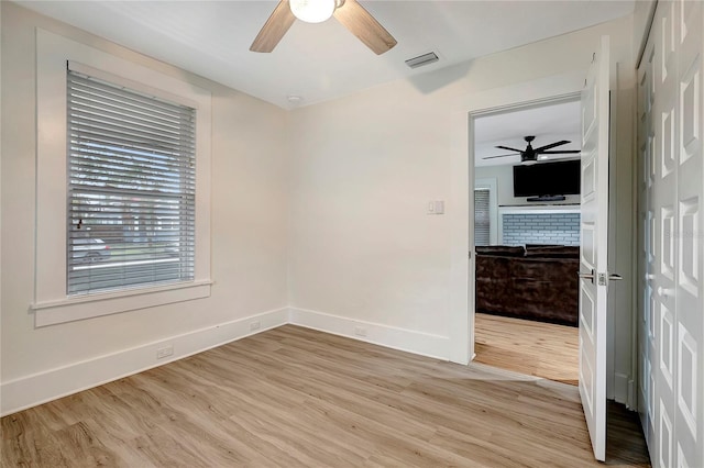 spare room with visible vents, a ceiling fan, light wood-type flooring, baseboards, and a brick fireplace