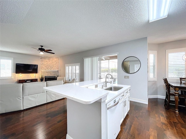 kitchen featuring dark hardwood / wood-style floors, a fireplace, an island with sink, sink, and white dishwasher