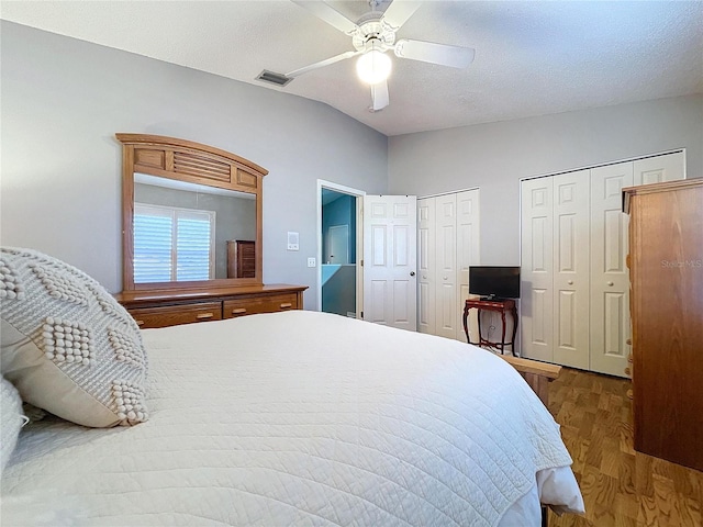 bedroom with lofted ceiling, hardwood / wood-style flooring, ceiling fan, a textured ceiling, and multiple closets