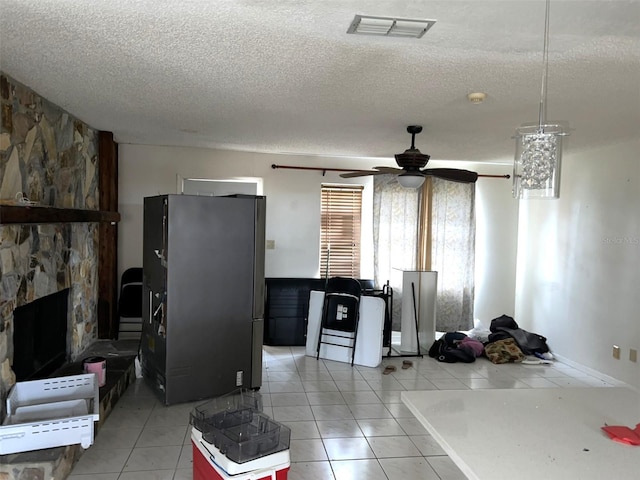 kitchen featuring stainless steel fridge, ceiling fan, a fireplace, light tile patterned flooring, and a textured ceiling