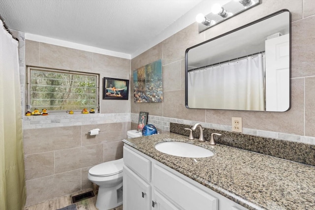 bathroom with vanity, toilet, tile walls, and a textured ceiling