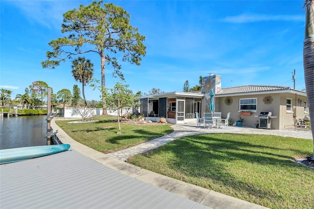 rear view of house featuring a patio area, a lawn, a sunroom, and a water view