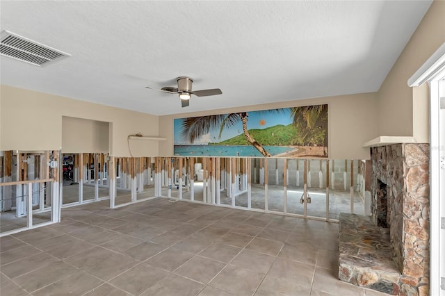 tiled empty room featuring a stone fireplace, a textured ceiling, and ceiling fan