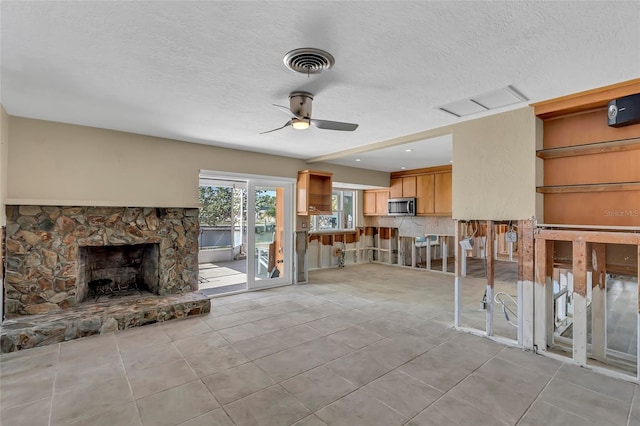 unfurnished living room with a stone fireplace, light tile patterned floors, a textured ceiling, and ceiling fan