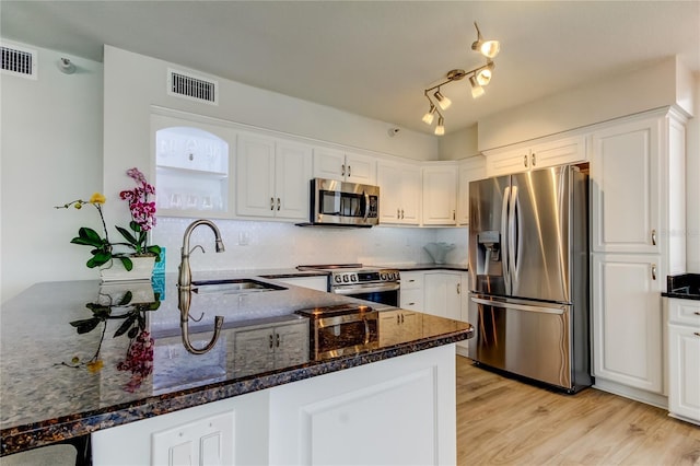 kitchen with sink, appliances with stainless steel finishes, kitchen peninsula, dark stone counters, and white cabinets