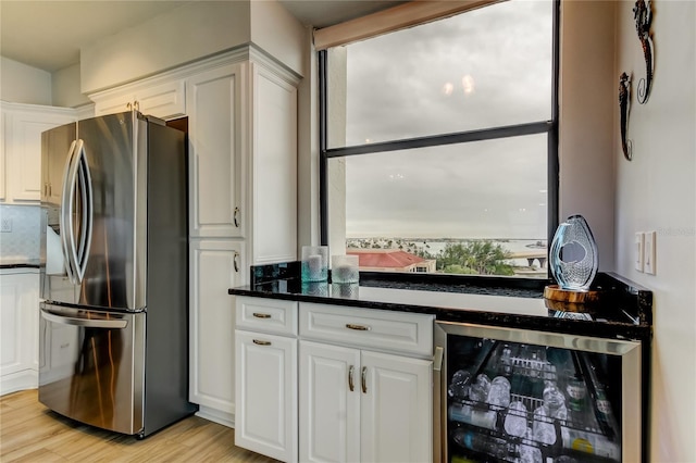 kitchen with white cabinetry, stainless steel fridge with ice dispenser, light hardwood / wood-style flooring, dark stone counters, and beverage cooler