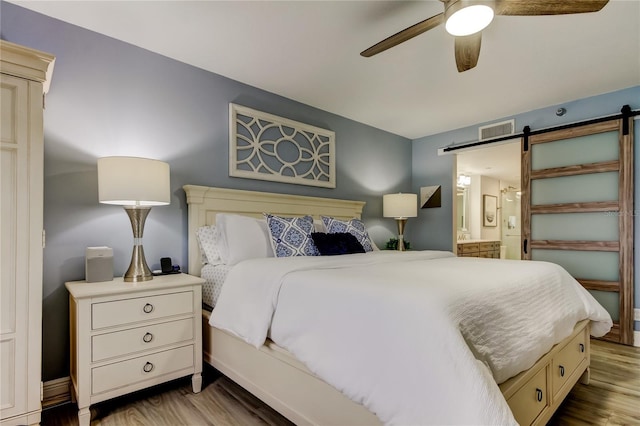 bedroom with ceiling fan, a barn door, ensuite bath, and light hardwood / wood-style floors