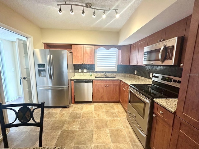 kitchen with sink, tasteful backsplash, light stone countertops, a textured ceiling, and stainless steel appliances