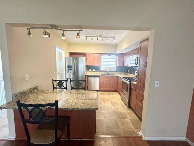 kitchen featuring light stone countertops, stainless steel appliances, sink, kitchen peninsula, and a breakfast bar