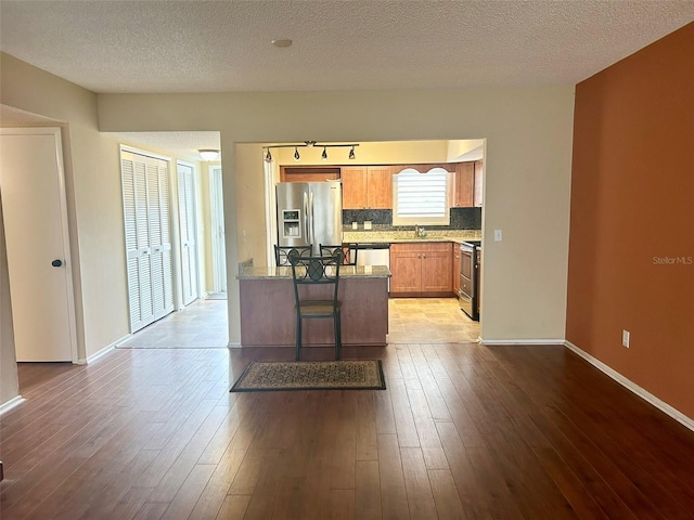 kitchen featuring light stone countertops, a textured ceiling, light hardwood / wood-style floors, a breakfast bar area, and stainless steel appliances