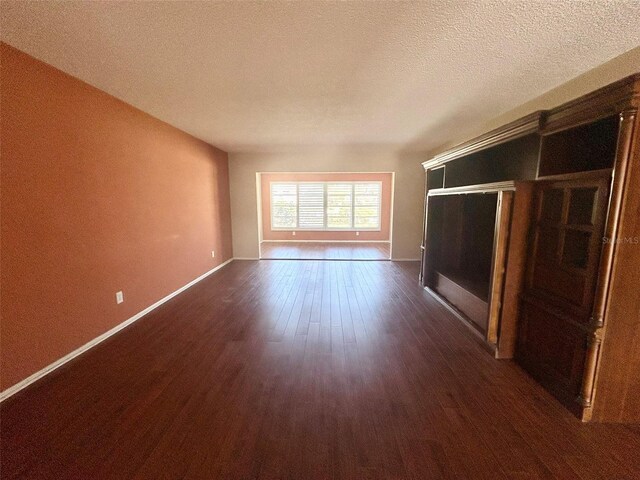 unfurnished living room with a textured ceiling, baseboards, and dark wood-type flooring