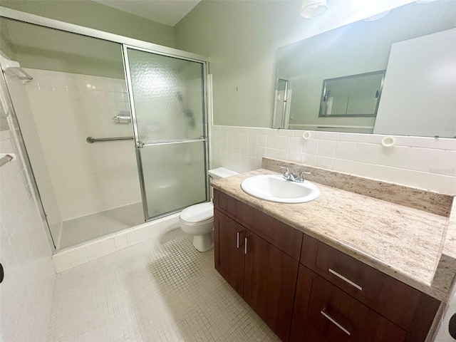 bathroom with a stall shower, toilet, tile patterned floors, vanity, and tile walls