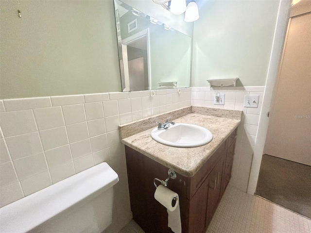 bathroom with visible vents, wainscoting, toilet, vanity, and tile walls