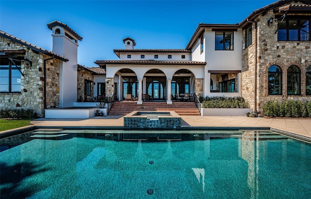 rear view of house featuring a tile roof, a patio, stucco siding, a pool with connected hot tub, and stone siding