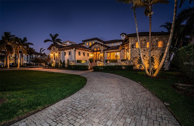 view of front of home with stone siding, curved driveway, and a lawn