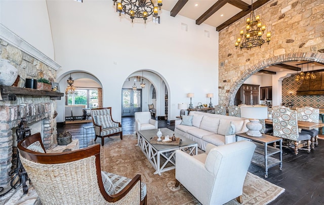 living area with arched walkways, a fireplace with raised hearth, a notable chandelier, wood finished floors, and beamed ceiling