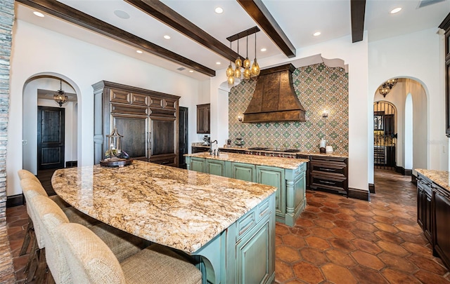 kitchen featuring arched walkways, a kitchen island with sink, custom exhaust hood, pendant lighting, and backsplash