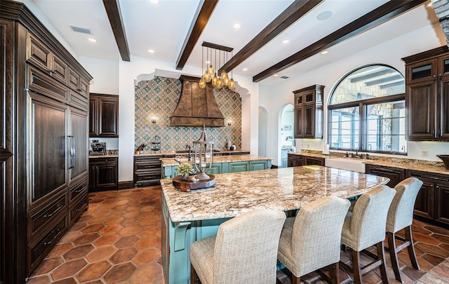 kitchen featuring a center island with sink, glass insert cabinets, light stone countertops, pendant lighting, and a sink