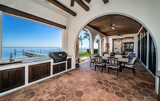 view of patio featuring a ceiling fan, a water view, a grill, outdoor dining area, and a sink