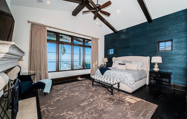 bedroom with an accent wall, wood finished floors, a water view, a fireplace, and beam ceiling