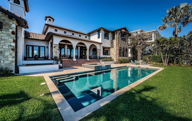 rear view of property with a patio, a pool with connected hot tub, stone siding, a lawn, and stucco siding