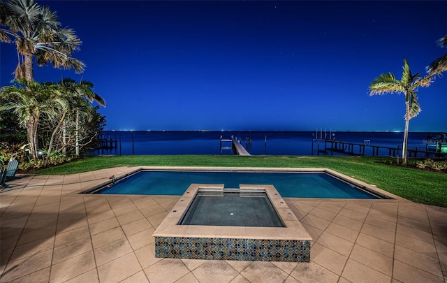 pool featuring an in ground hot tub, a patio, a lawn, and a water view