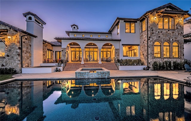 rear view of house with an in ground hot tub, stucco siding, an outdoor pool, and a patio