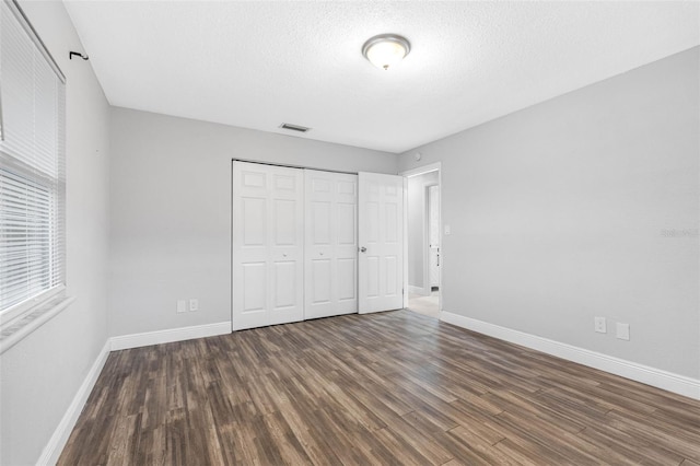 unfurnished bedroom featuring dark wood-type flooring, a textured ceiling, and a closet