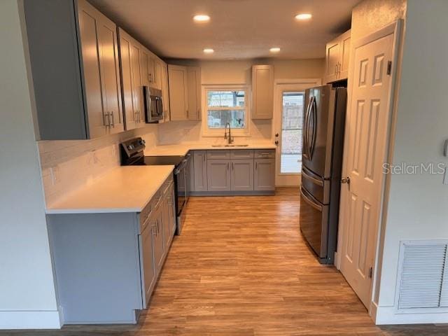 kitchen with sink, appliances with stainless steel finishes, gray cabinetry, and light wood-type flooring