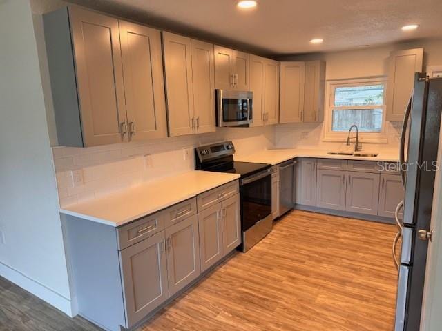 kitchen with appliances with stainless steel finishes, gray cabinetry, sink, light wood-type flooring, and backsplash