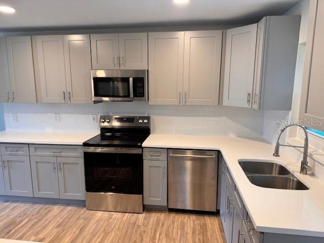 kitchen with light hardwood / wood-style flooring, sink, backsplash, gray cabinetry, and stainless steel appliances