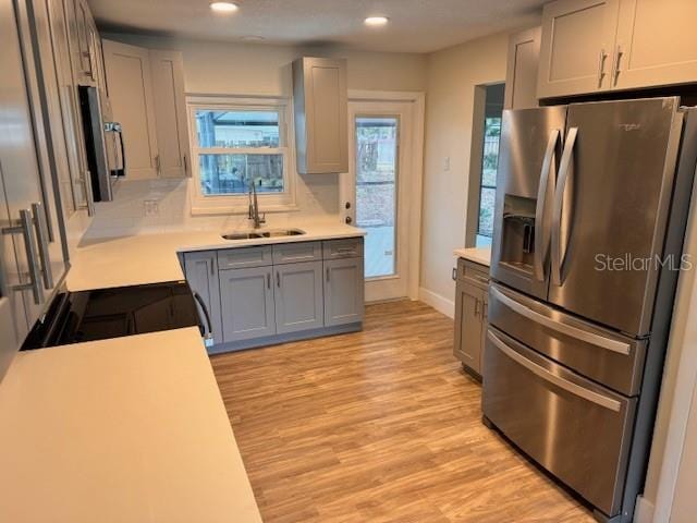 kitchen with appliances with stainless steel finishes, sink, backsplash, light wood-type flooring, and gray cabinets