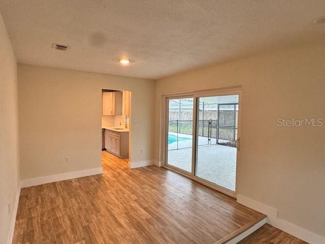 spare room with sink, light hardwood / wood-style floors, and a textured ceiling