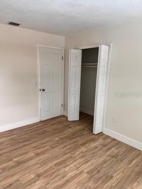 unfurnished bedroom with hardwood / wood-style floors, a textured ceiling, and a closet