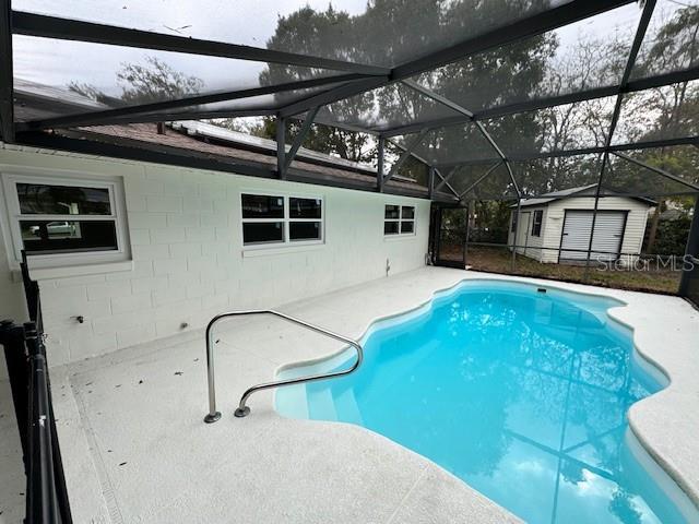 view of swimming pool featuring a lanai and a storage shed