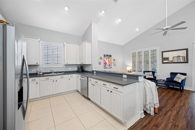 kitchen with vaulted ceiling, decorative backsplash, white cabinets, kitchen peninsula, and stainless steel appliances