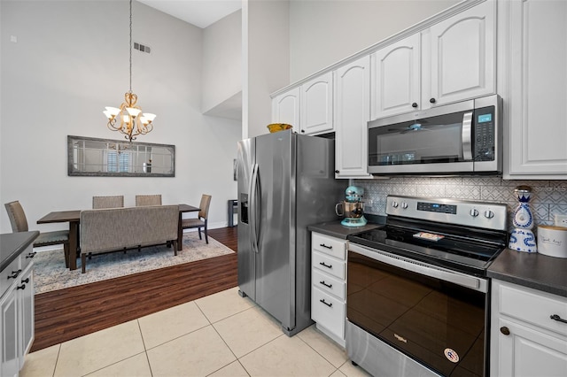 kitchen featuring pendant lighting, white cabinets, appliances with stainless steel finishes, a towering ceiling, and light tile patterned flooring