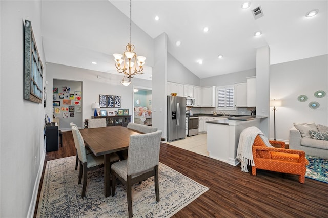 dining area featuring light hardwood / wood-style floors, high vaulted ceiling, and a notable chandelier