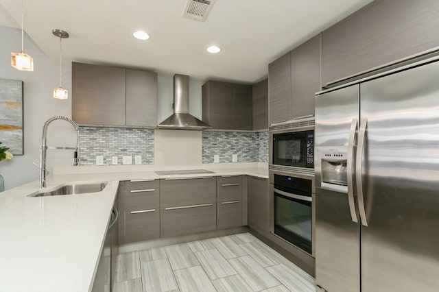 kitchen with black appliances, hanging light fixtures, decorative backsplash, sink, and wall chimney exhaust hood