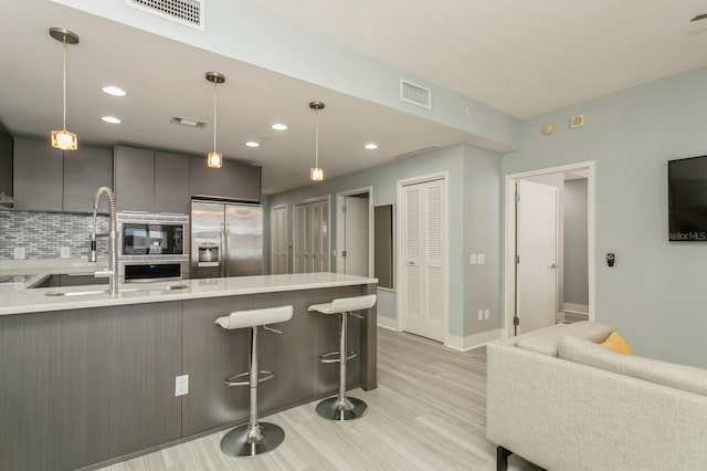 kitchen featuring built in appliances, decorative backsplash, a kitchen breakfast bar, light hardwood / wood-style flooring, and pendant lighting