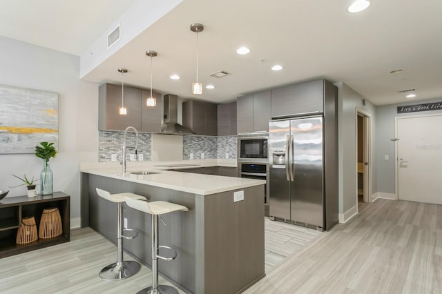 kitchen featuring pendant lighting, black appliances, a kitchen breakfast bar, kitchen peninsula, and wall chimney range hood