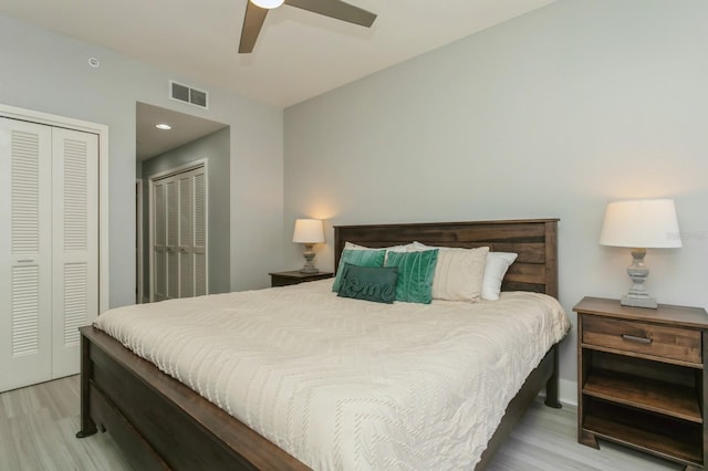 bedroom featuring two closets, light hardwood / wood-style floors, and ceiling fan