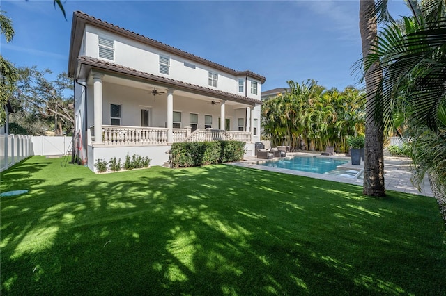 back of property with ceiling fan, a patio area, a fenced in pool, and a lawn