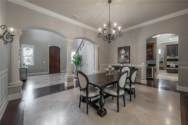 dining area featuring ornamental molding, ornate columns, a notable chandelier, and beverage cooler