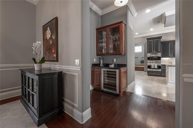 bar featuring dark hardwood / wood-style flooring, double oven, ornamental molding, and wine cooler