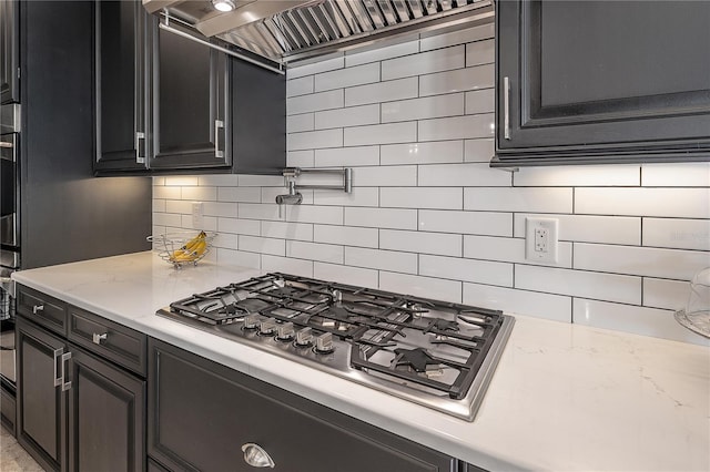 kitchen featuring wall chimney exhaust hood, backsplash, light stone countertops, and stainless steel gas cooktop